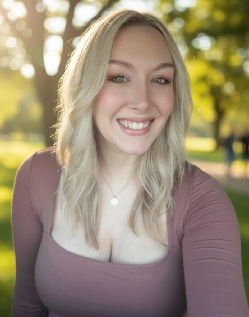 blonde woman smiling in black blazer and a white shirt with a grayish blue background
